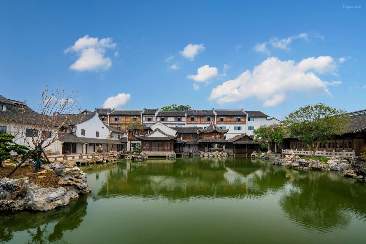 A traditional Chinese courtyard with white walls, tiled roofs, and a calm water feature reflecting the surrounding architecture.