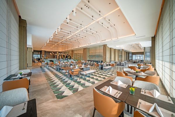 A spacious restaurant interior with high ceilings, soft neutral tones, and rows of neatly arranged dining tables.