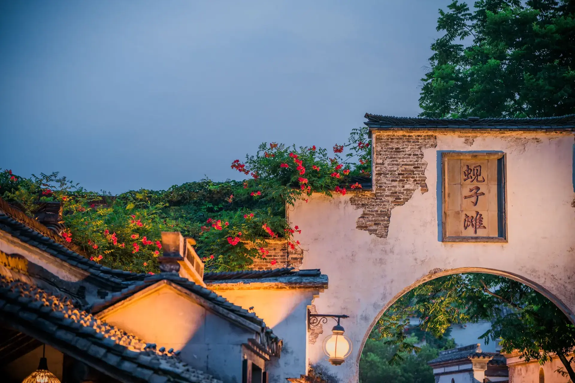 White wall archway with "Xianzitan" plaque and red flowers.
