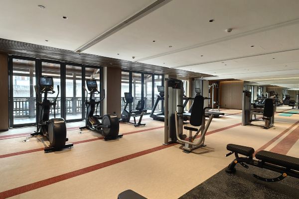 A modern hotel gym with floor-to-ceiling windows, equipped with treadmills, weights, and fitness machines.