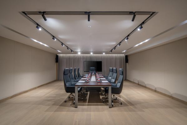 A minimalist meeting room with a long table, comfortable chairs, and soft lighting for business or private gatherings.