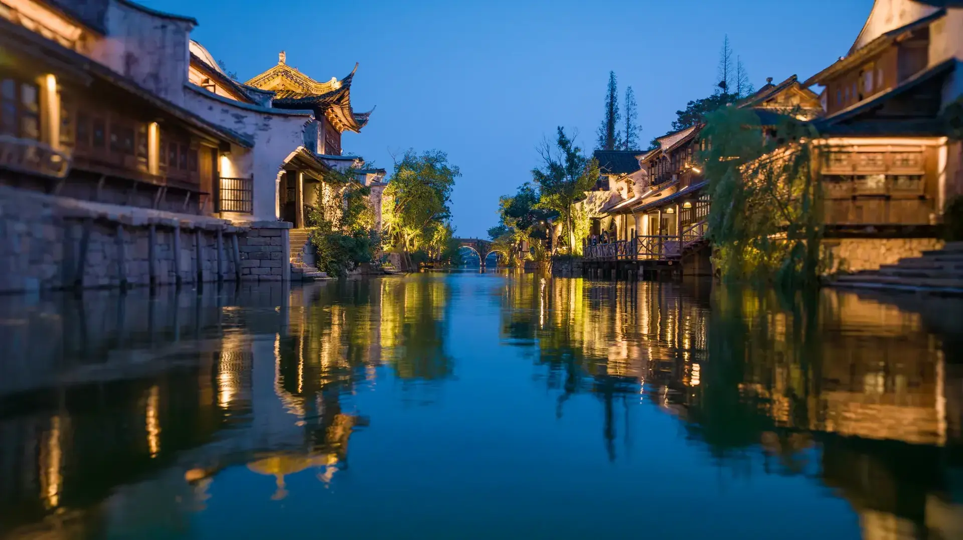 Illuminated waterside houses reflecting on calm canal at twilight.