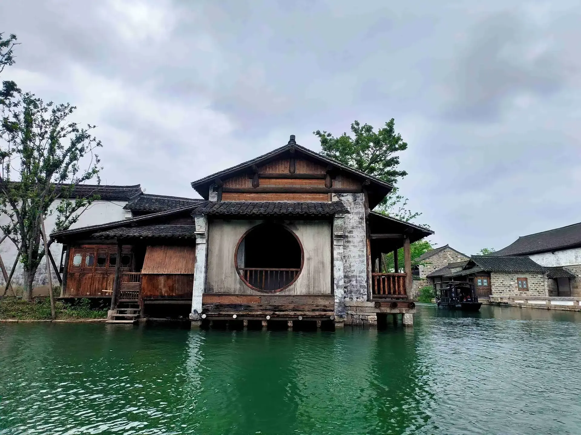 Traditional stilt building with circular window by green canal.