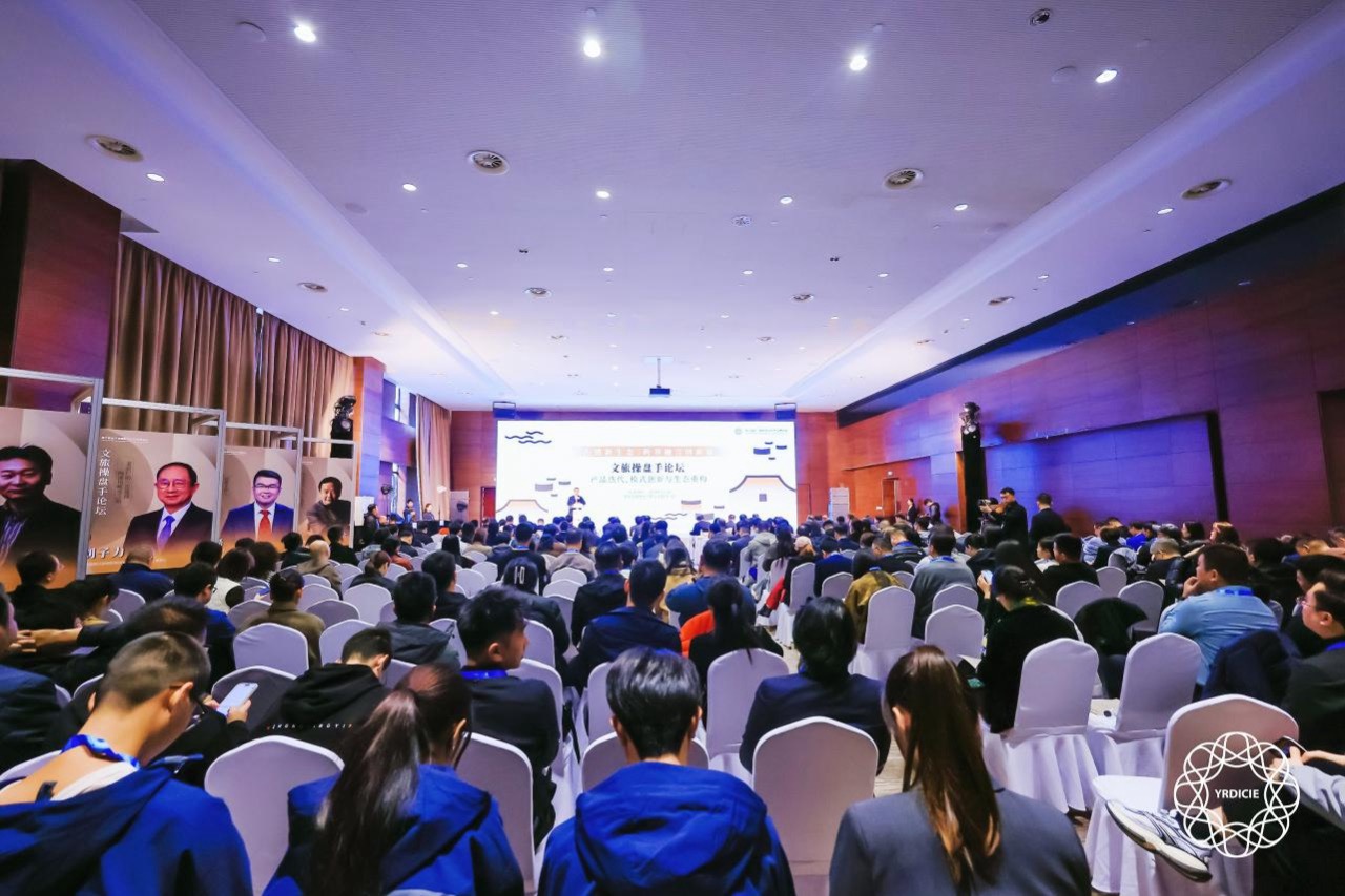 Large conference hall packed with attendees for cultural tourism asset operation forum, stage screen and speaker portraits on side display boards.