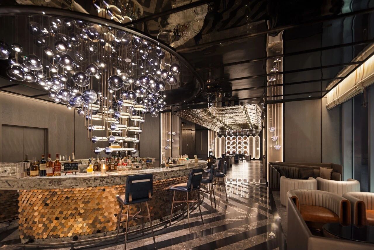 Curved cocktail bar covered in brass mosaic, huge bubble glass pendant installation overhead.