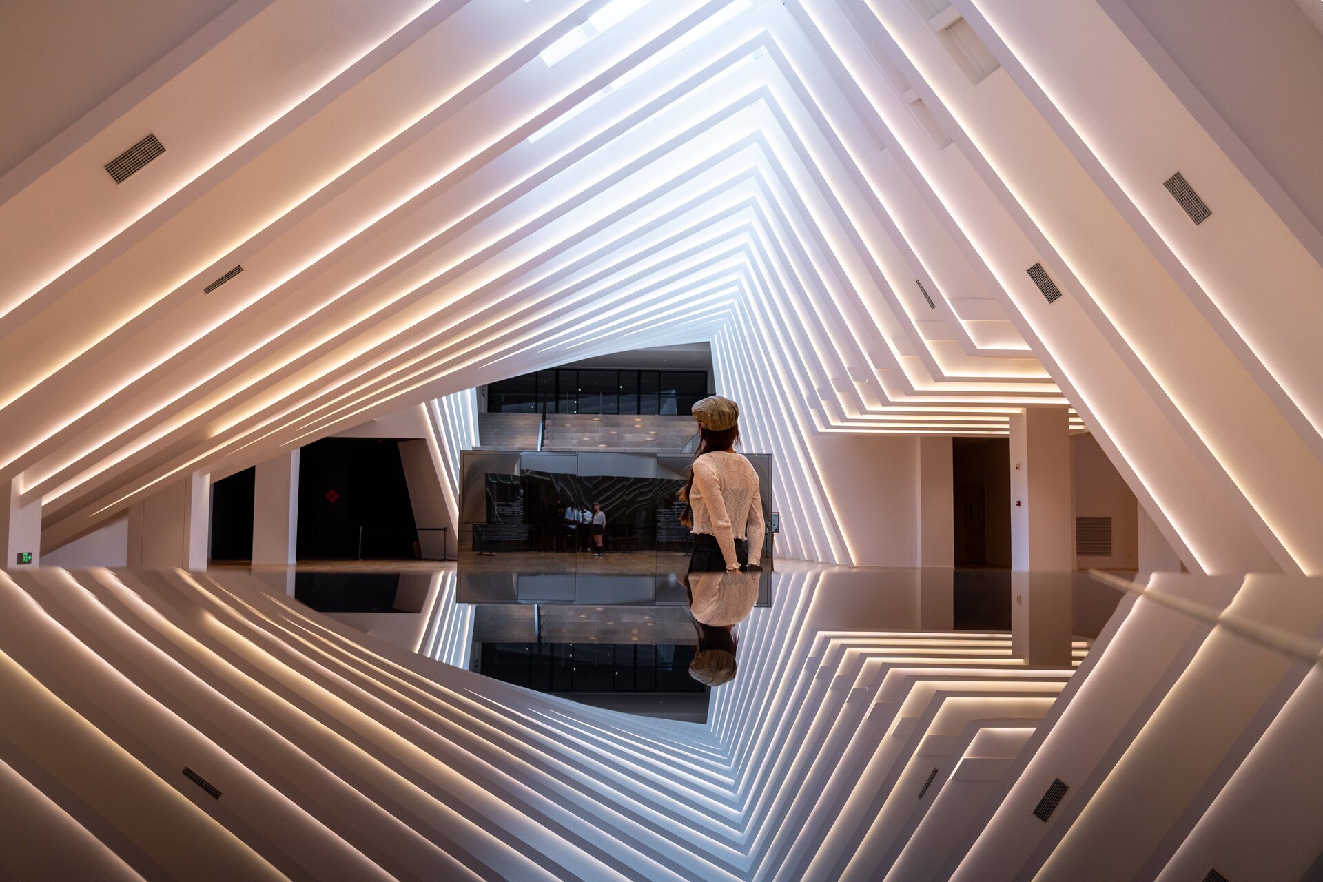 Wide shot of angular white layered ceiling lobby with central white service counter and museum logo on glass partition.