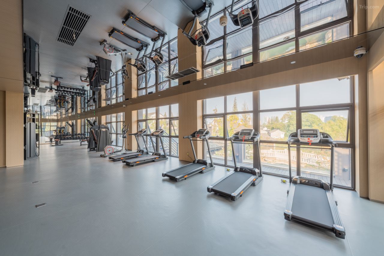 Well-equipped gym lined with treadmills, large floor windows overlooking ancient town greenery.