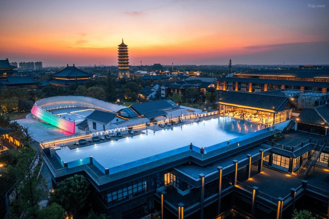 Rooftop infinity pool at dusk, overlooking Puyuan ancient town pagoda and tiled Huizhou buildings under gradient sunset sky.