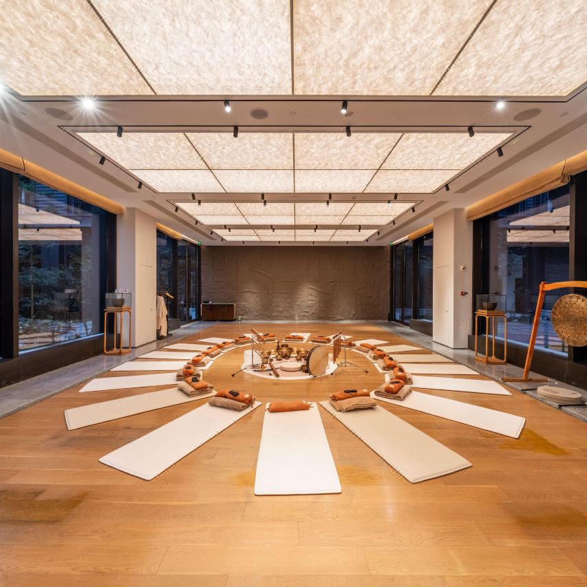 Bright yoga room laid with beige mats, central sound therapy instrument and fabric skylight ceiling.