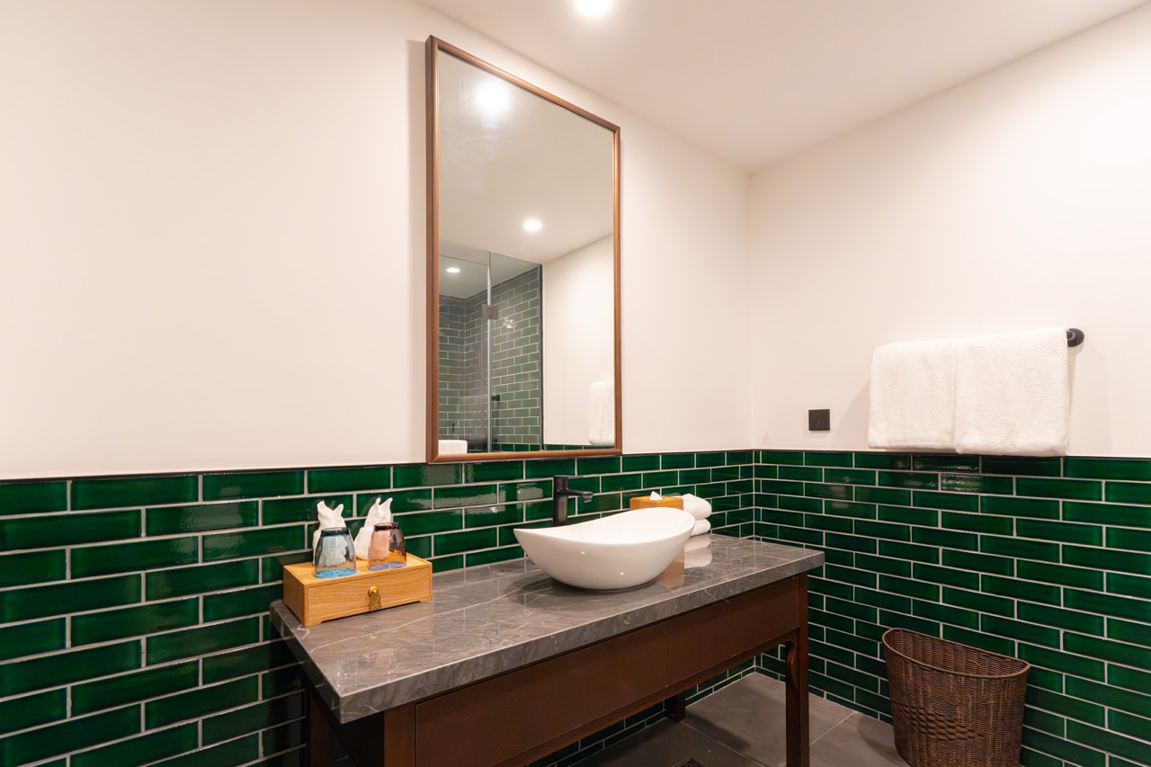 Dark wood vanity with marble top, oval mirror, white basin and woven storage basket.