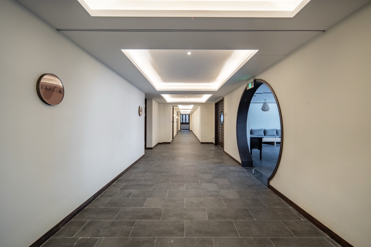 Minimalist hotel corridor with recessed ceiling lighting, grey tile floor and Chinese round moon door.