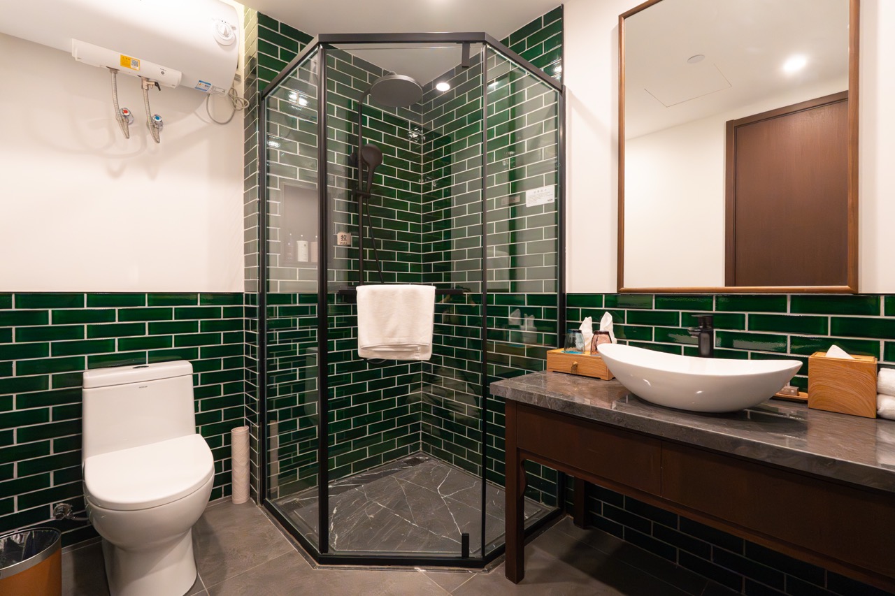Bathroom with glass enclosed shower stall, white toilet, glossy green tile walls and bath amenities.