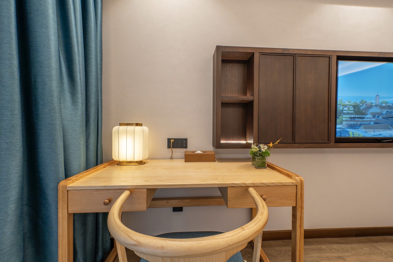 Natural wood desk with fabric lamp, built-in cabinet, blue curtain and window overlooking ancient town.