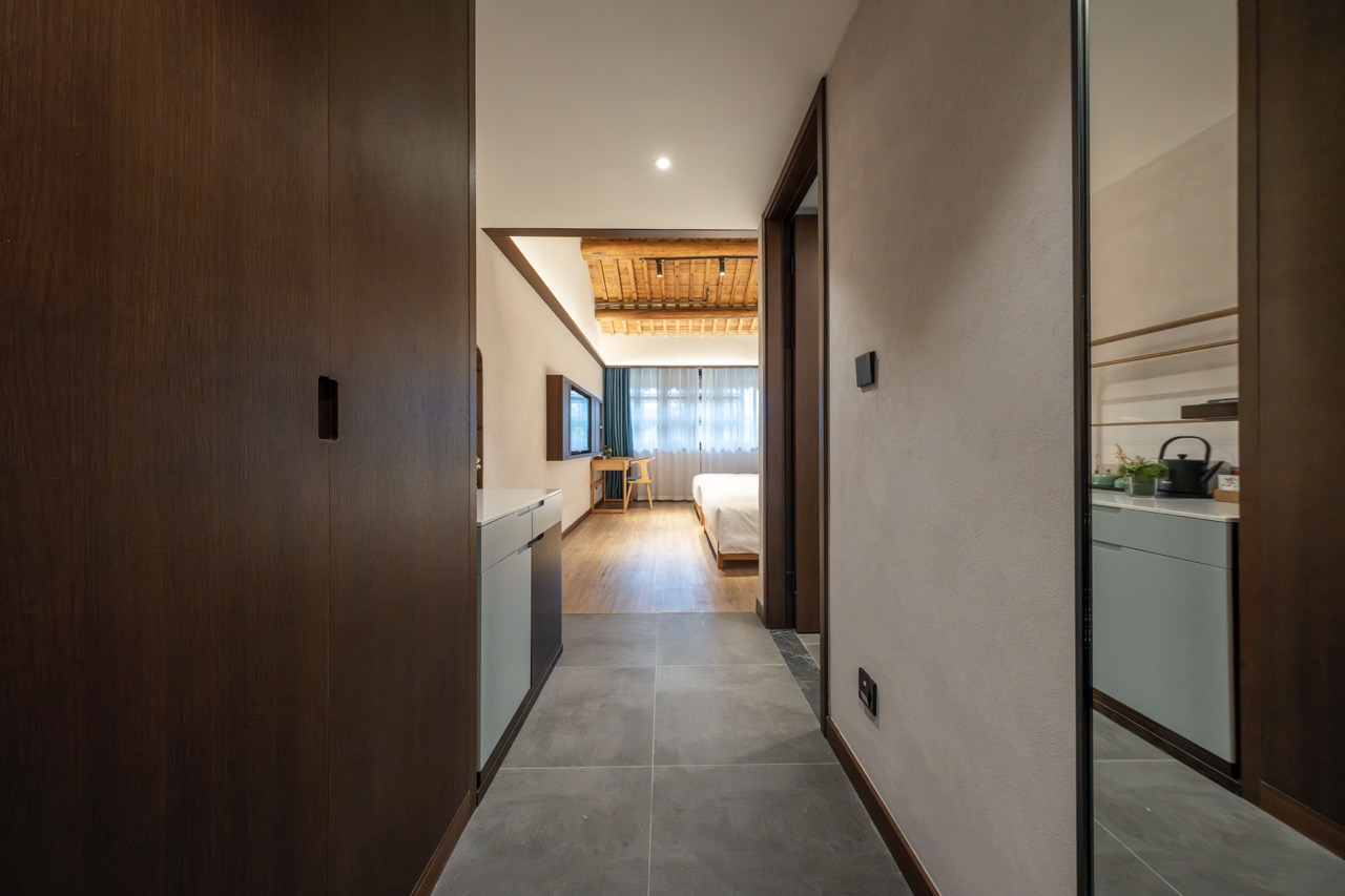 Room entrance with dark timber sliding doors, vanity counter, wooden bed and warm rustic ceiling beams.