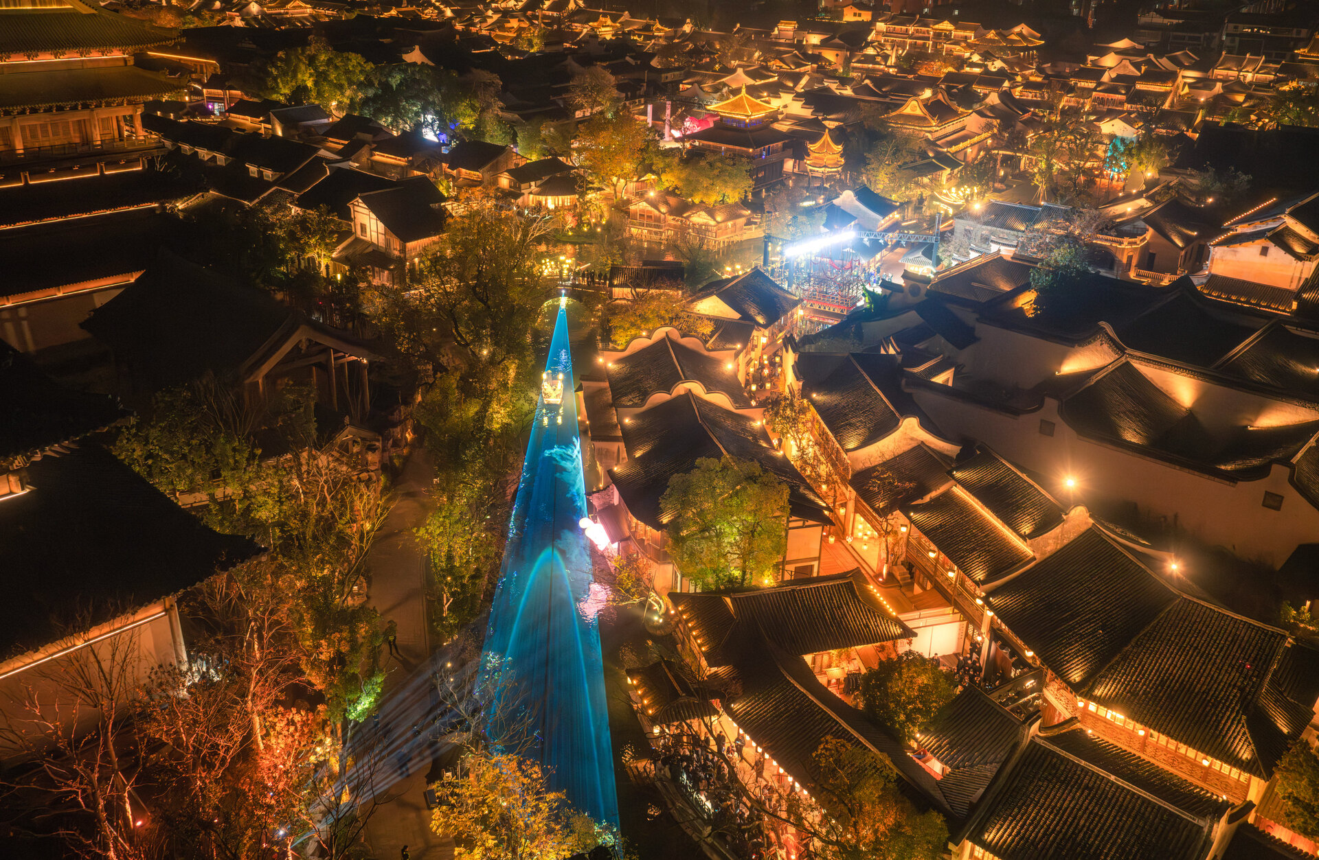 Aerial night view of Puyuan water town illuminated during the GQ Annual Awards ceremony, with traditional rooftops, glowing lights, and a central canal highlighted by blue lighting installations.
