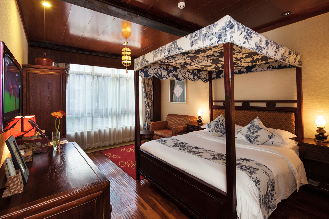 Interior of a deluxe balcony double room with carved wooden bed.