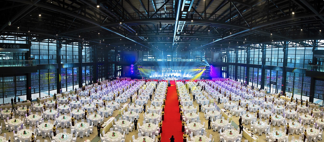 Huge exhibition hall transformed into banquet venue with central red carpet stage for international summit dinner.