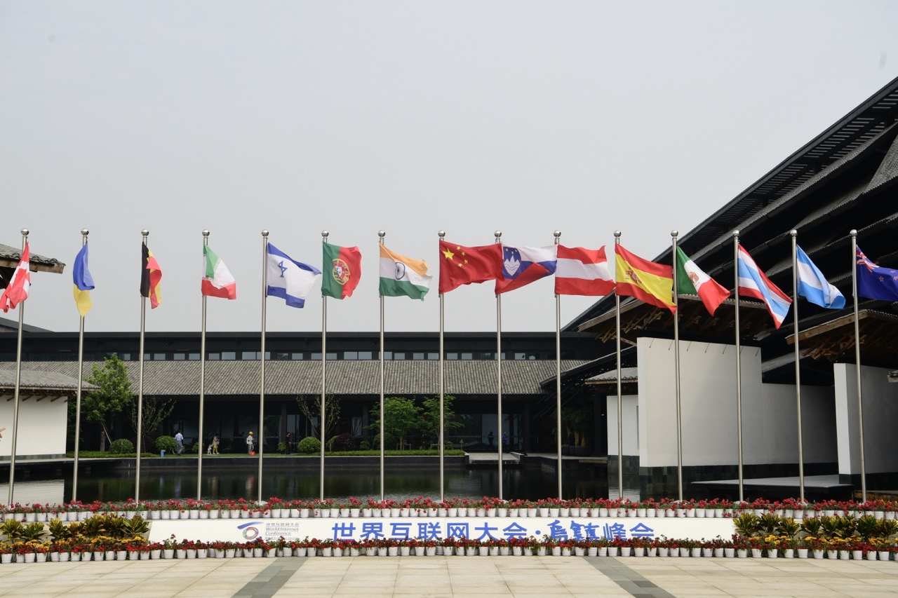 Plaza lined with national flags for World Internet Conference Wuzhen Summit, traditional waterside architecture backdrop.