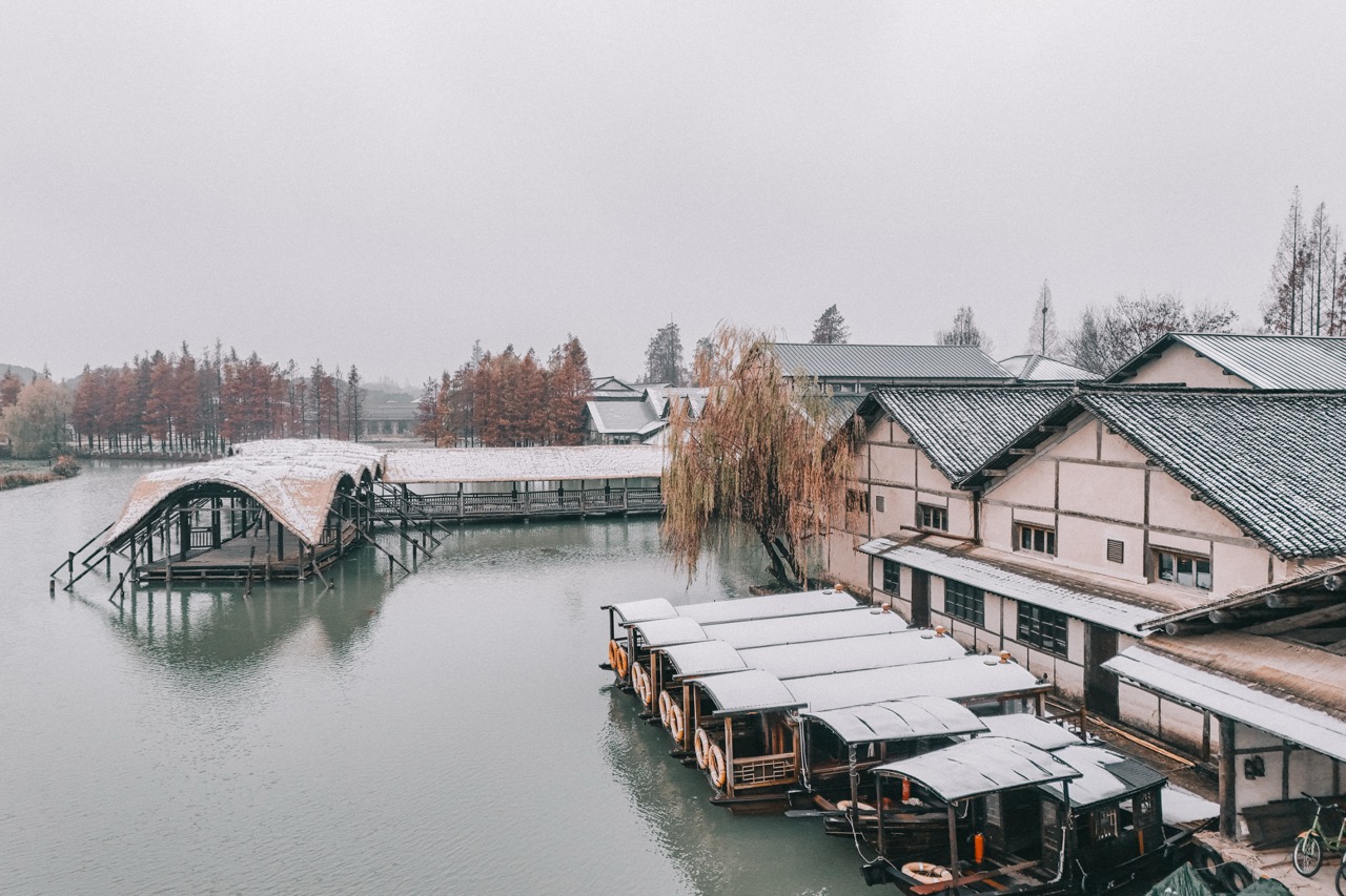 Snow dusted wooden sightseeing boats and old timber buildings along misty canal on cold snowy day.