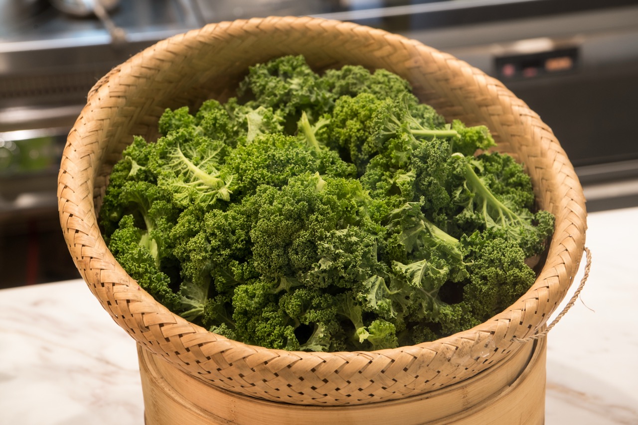Vibrant green kale neatly placed inside hand-woven rattan basket over bamboo steamer.