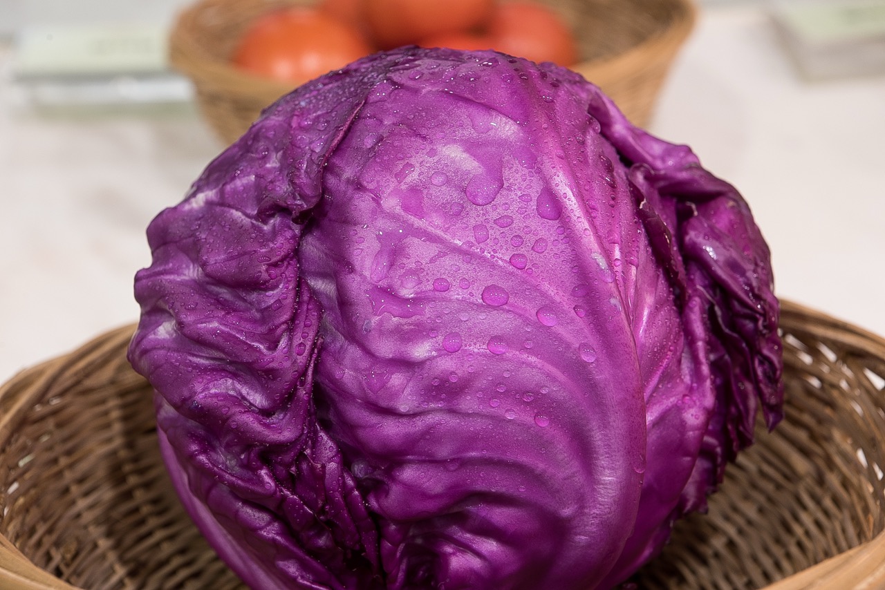 Whole purple cabbage covered with water droplets laid in wicker basket.