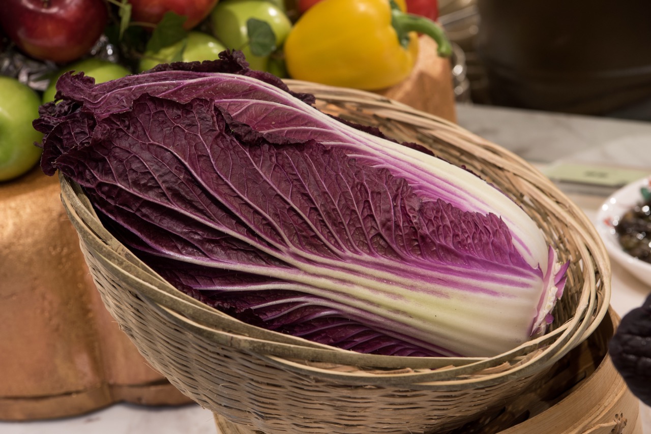 Fresh purple leaf Chinese cabbage with gradient purple veins displayed in bamboo basket.