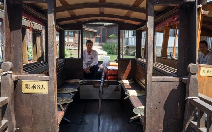 Wooden passenger cabin of traditional canal boat, marked with "Max 8 Passengers" sign and folding palm fans on benches.