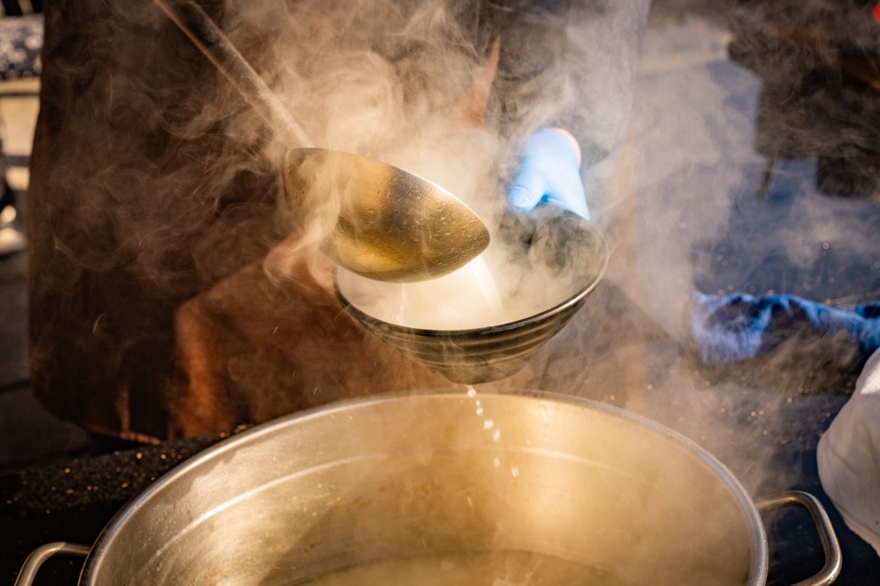 Metal spoon pouring boiling soup with thick white steam rising up.