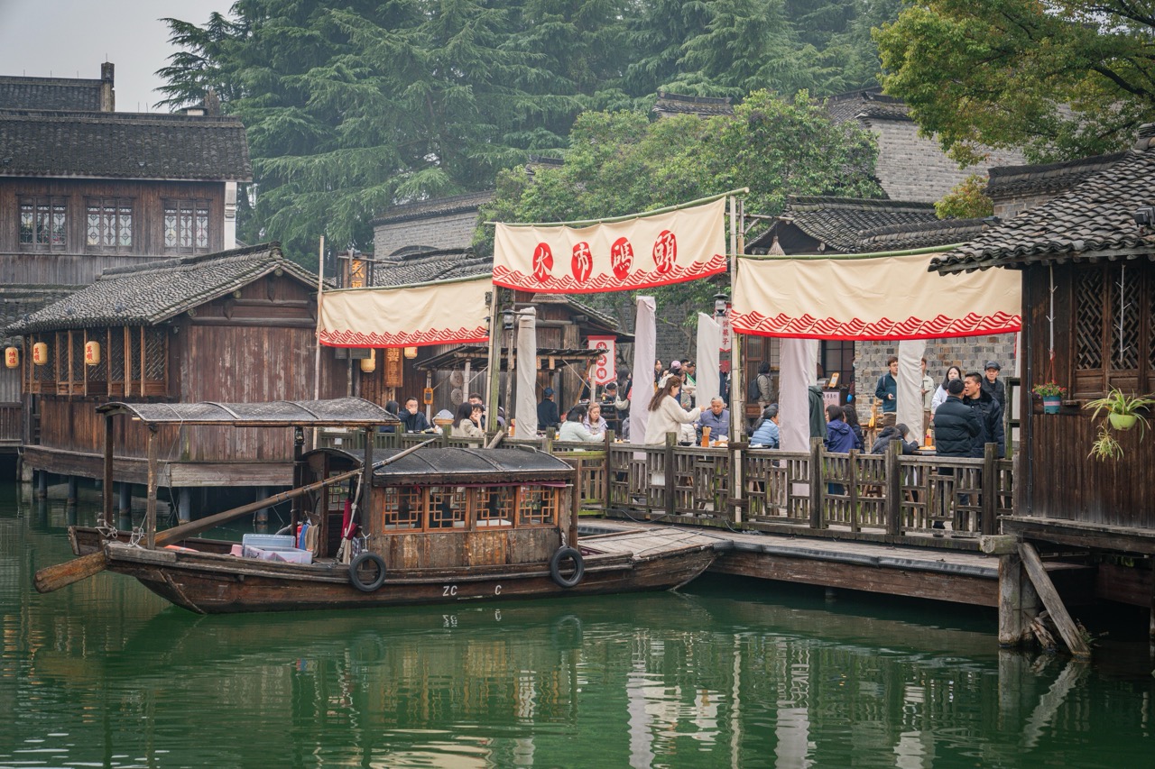 Wooden tour boat docked beside overwater teahouses with red banner "Water Market".