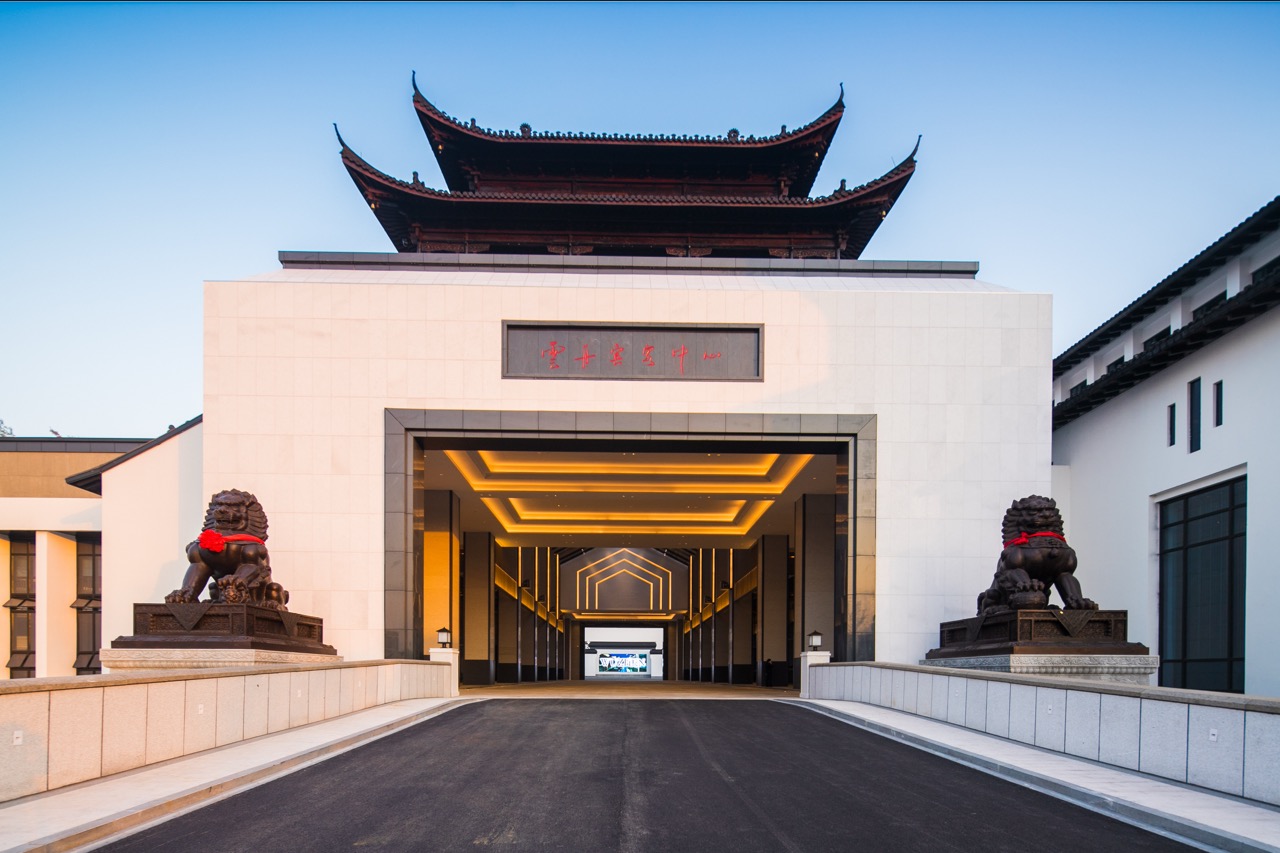 Entrance facade of Yunzhou Guest Center, blending ancient Chinese tower roof and modern minimalist wall with bronze lion statues.