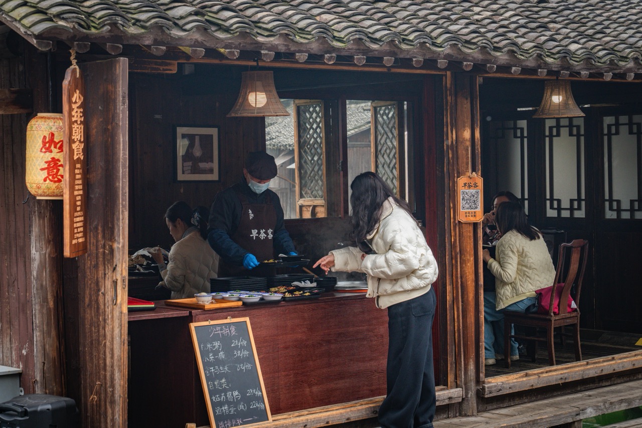 Old timber teahouse stall with menu blackboard, staff serving customers at counter.