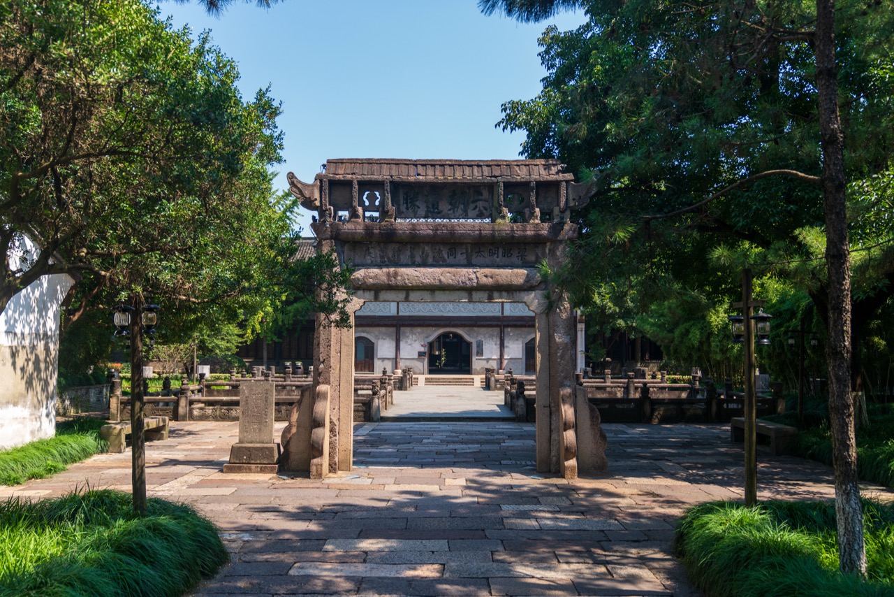 Historic stone memorial archway leading into Zhaoming Academy, surrounded by lush old trees.
