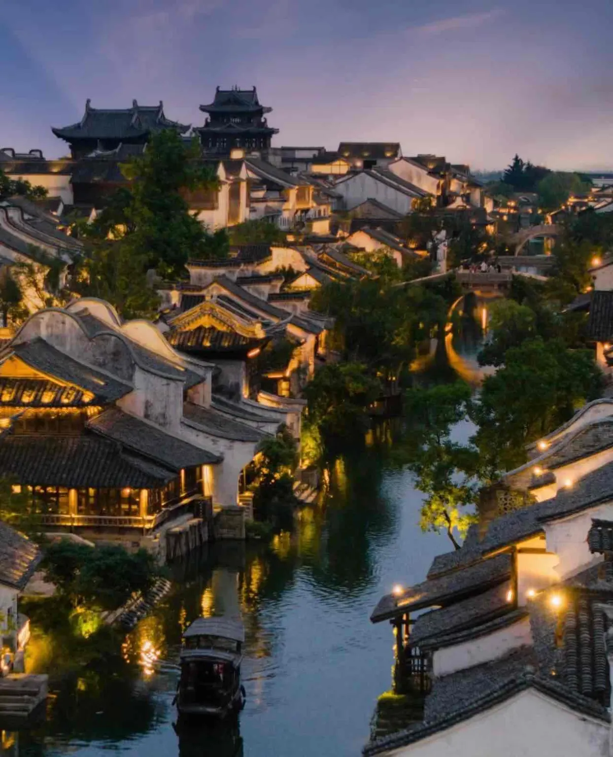 Twilight aerial view of lit riverside houses and boat in Yanguan old town。