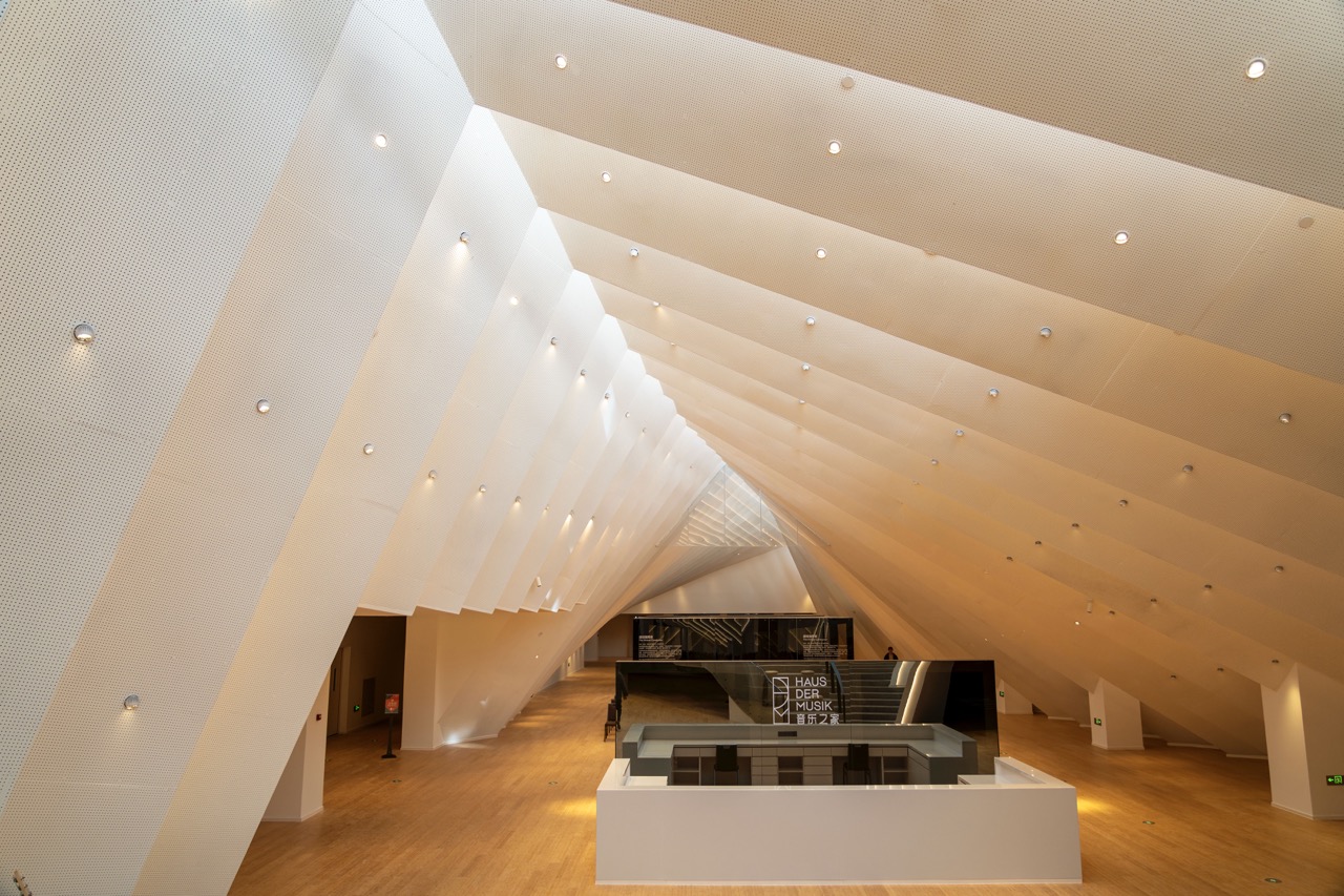 Wide shot of angular white layered ceiling lobby with central white service counter and museum logo on glass partition.