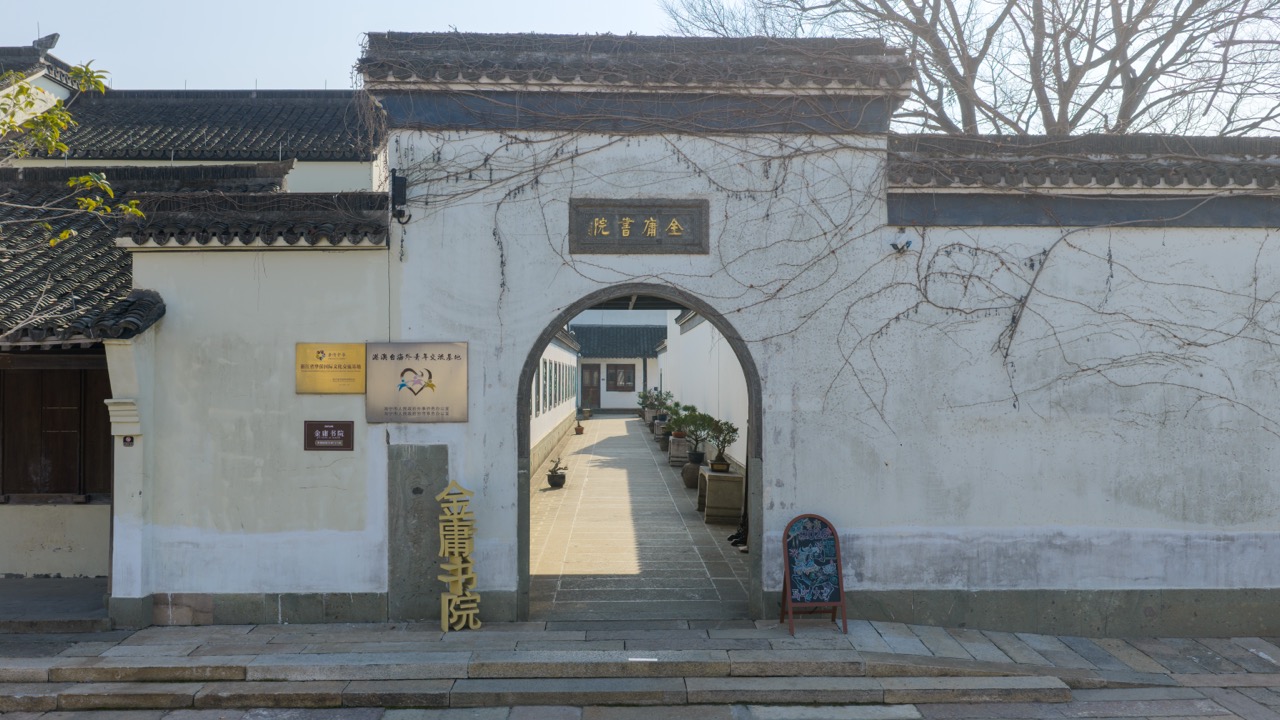 White plaster wall with curved moon arch, golden "Jin Yong Academy" sign on lintel.