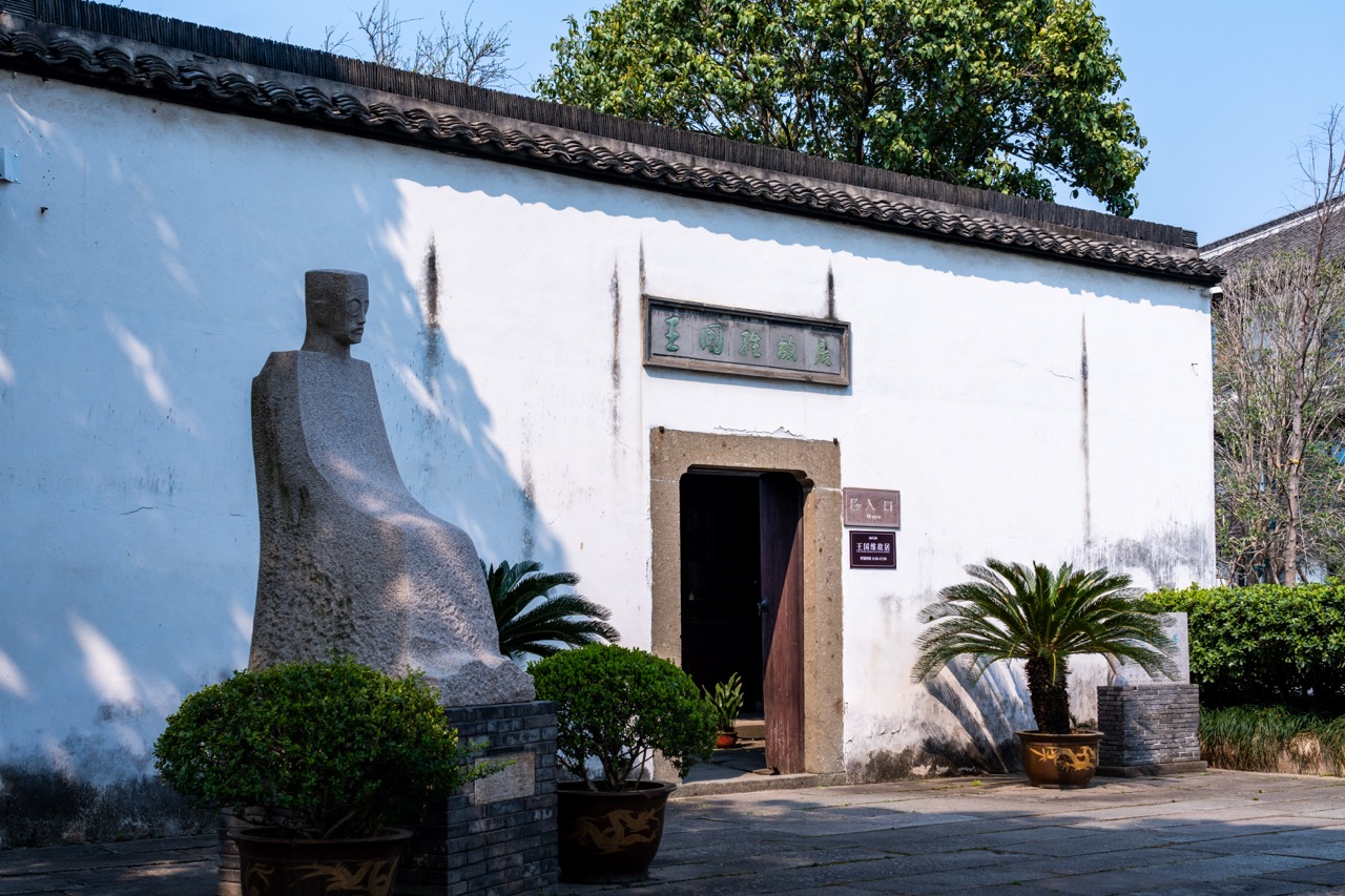 White Hu-style wall gate with stone statue of scholar Wang Guowei beside doorway.
