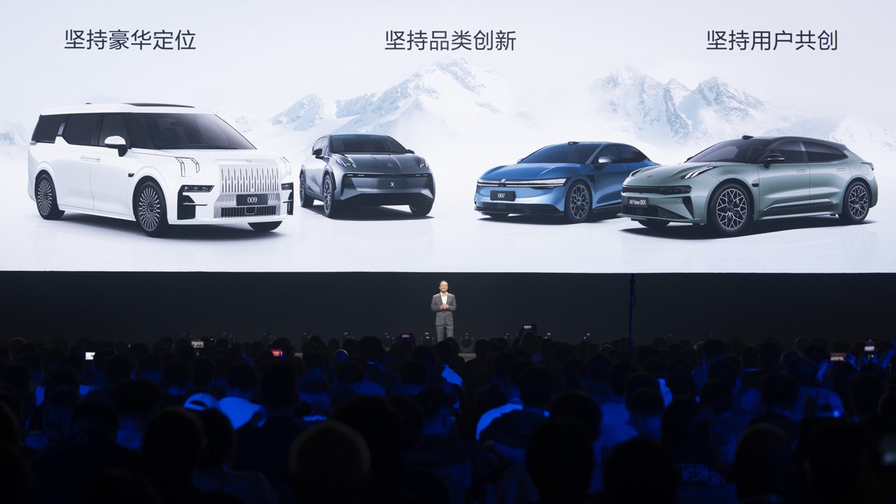 Keynote speaker on stage with huge screen showing full Zeekr vehicle lineup, large audience at auto new product launch conference held in Wuzhen.